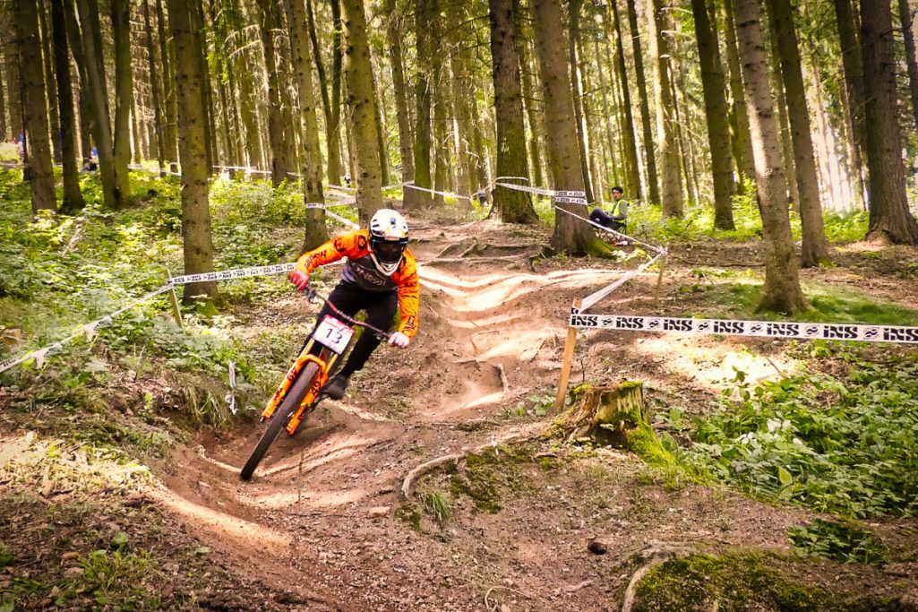 Mountainbiker in orange Rennanzug kurvt durch einen Waldpfad.
