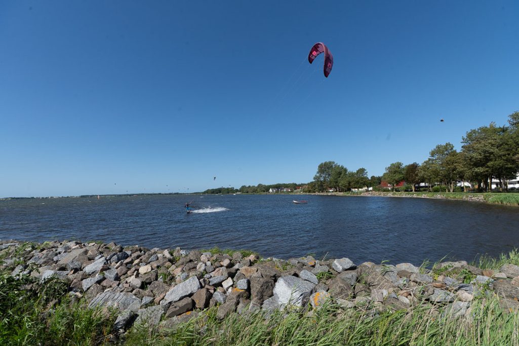 Kitesurfer auf ruhigem Gewässer mit einem klaren blauen Himmel im Hintergrund.