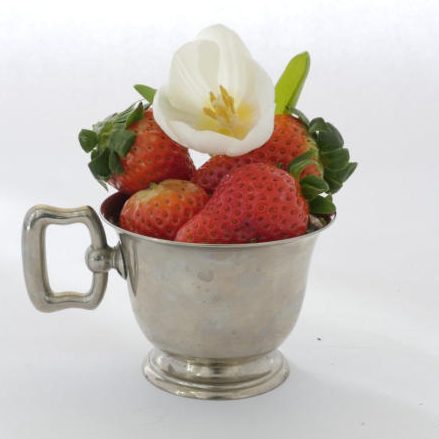 Silberne Tasse mit frischen Erdbeeren und einer weißen Blüte.
