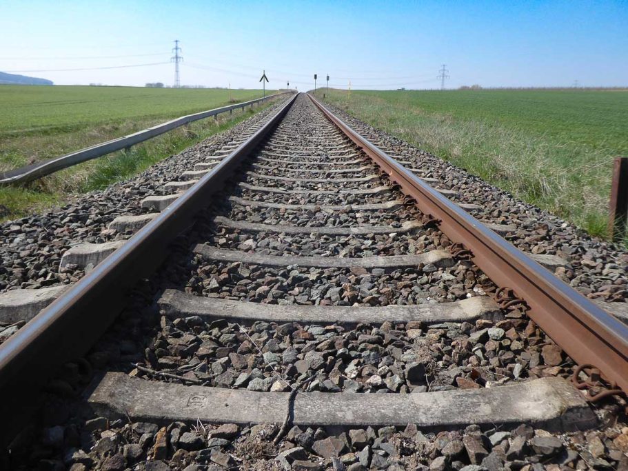 Eisenbahnschienen, die in die Ferne führen, umgeben von offenen Feldern.