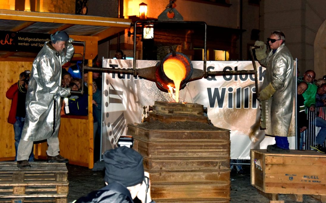 Zwei Personen in Schutzkleidung gießen geschmolzenes Metall an einem Arbeitsplatz. Metallgestaltertreffen in Gotha