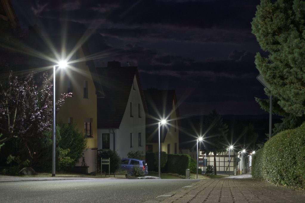 Nachtaufnahme einer ruhigen Straße mit beleuchteten Hausfassaden und Straßenlaternen.