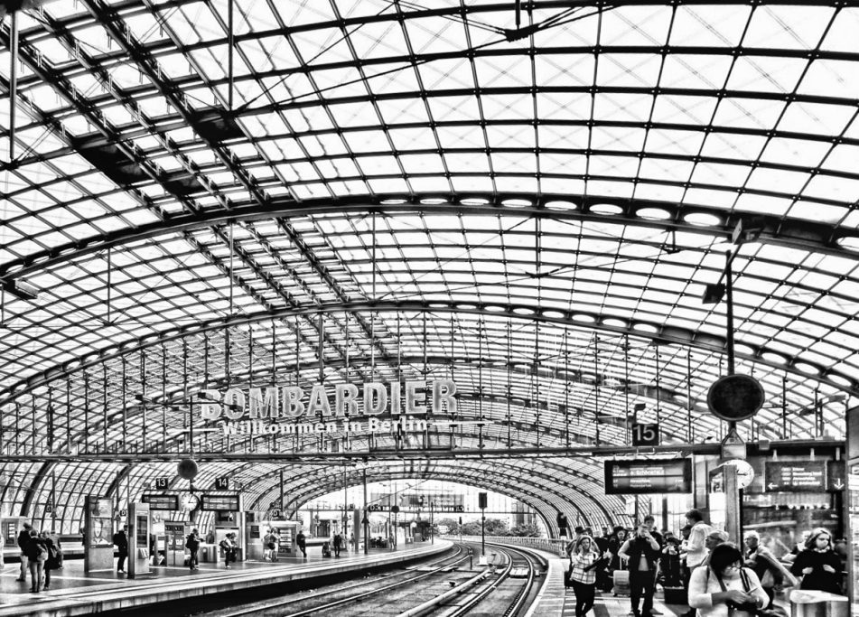 Architektonische Innenansicht eines Bahnhofs mit hohen Glasdecken und Gleisen.