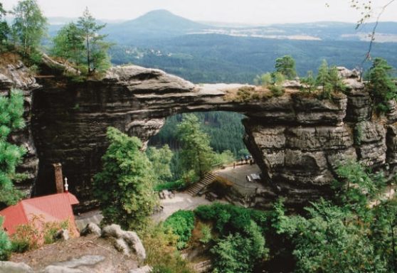 Naturfelsbogen umgeben von Bäumen, mit weitem Blick auf die Landschaft im Hintergrund.
