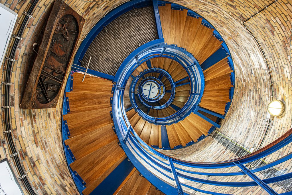 Eine spiralförmige Treppe aus Holz und blauen Geländern in einem Ziegelturm.