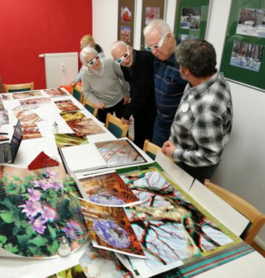 Personen betrachten verschiedene Kunstwerke auf einem Tisch in einem Raum mit roten Wänden.