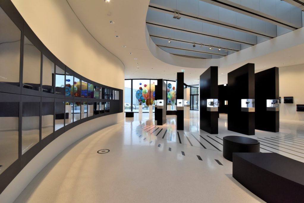 Moderne Galerie mit geschwungenen Wänden, schwarzen Podesten und bunten Kunstwerken.