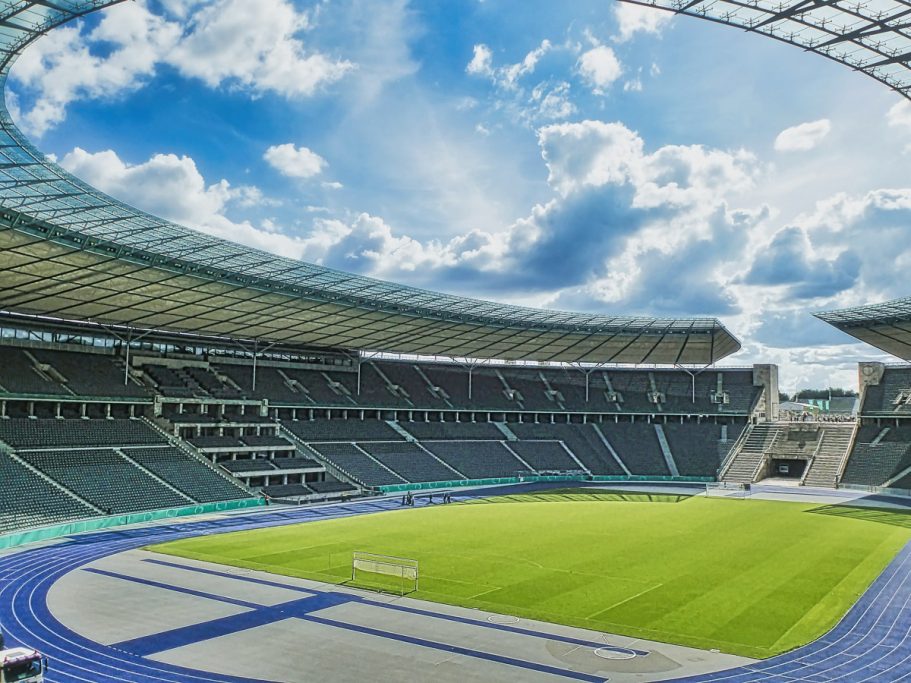 Großes Stadion mit grünem Rasen, blauen Laufbahnen und bewölktem Himmel.
