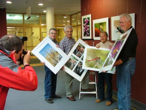Vier Personen halten gerahmte Fotos, während ein Fotograf sie ablichtet.