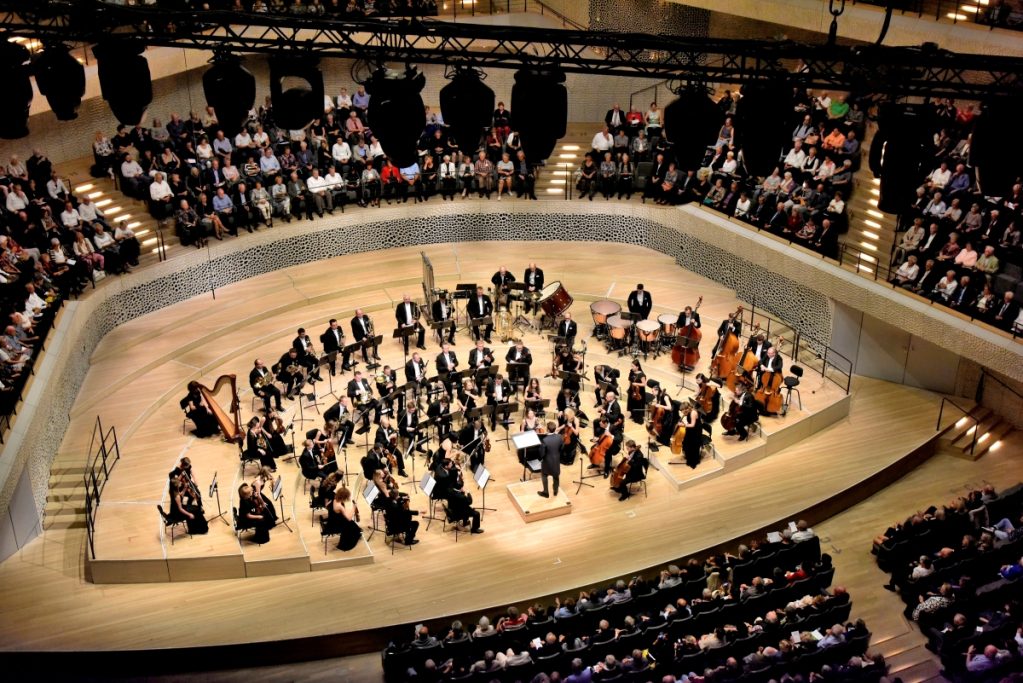 Orchester spielt auf einer beeindruckenden Bühne vor einem Publikum. Innenaufnahme der Elphi