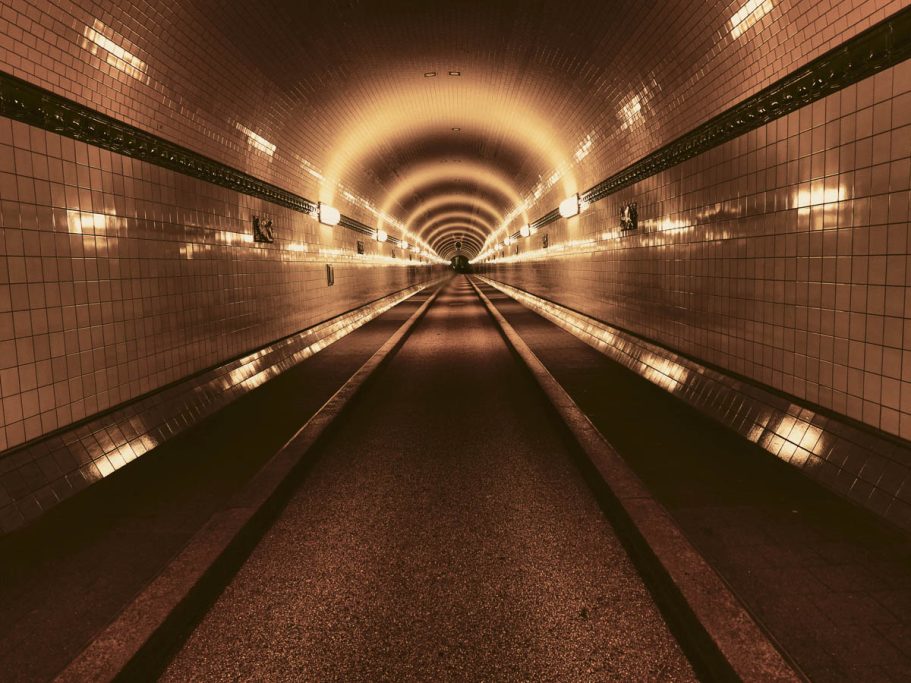 Ein beleuchteter Tunnel mit reflektierendem Boden und geschwungenen Wänden.